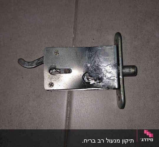 מנגנון מנעול כספת מתכתי מפורק עם סימני קידוח המונח על הרצפה